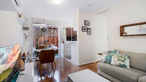 A modern living room with a flat-screen TV, a sofa, and a dining area with a table and chairs. - Snug St Kilda Apartment With Private Courtyard (Melbourne)