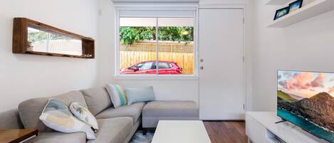 A modern living room with a sectional sofa, a flat-screen TV, and a sliding glass door leading to a backyard.