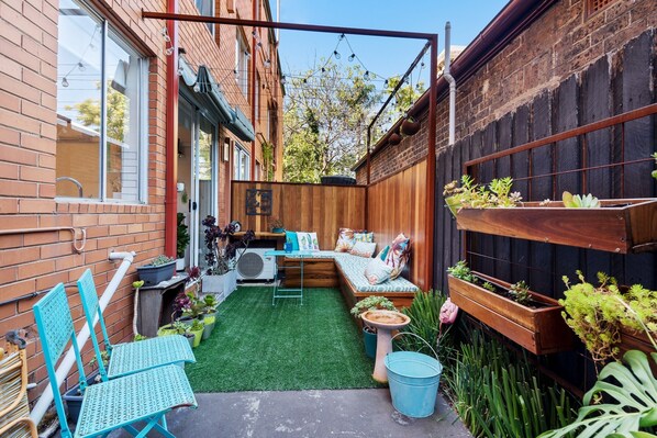 A small backyard with a wooden bench, a small table, and a variety of potted plants. - Snug St Kilda Apartment With Private Courtyard (Melbourne)