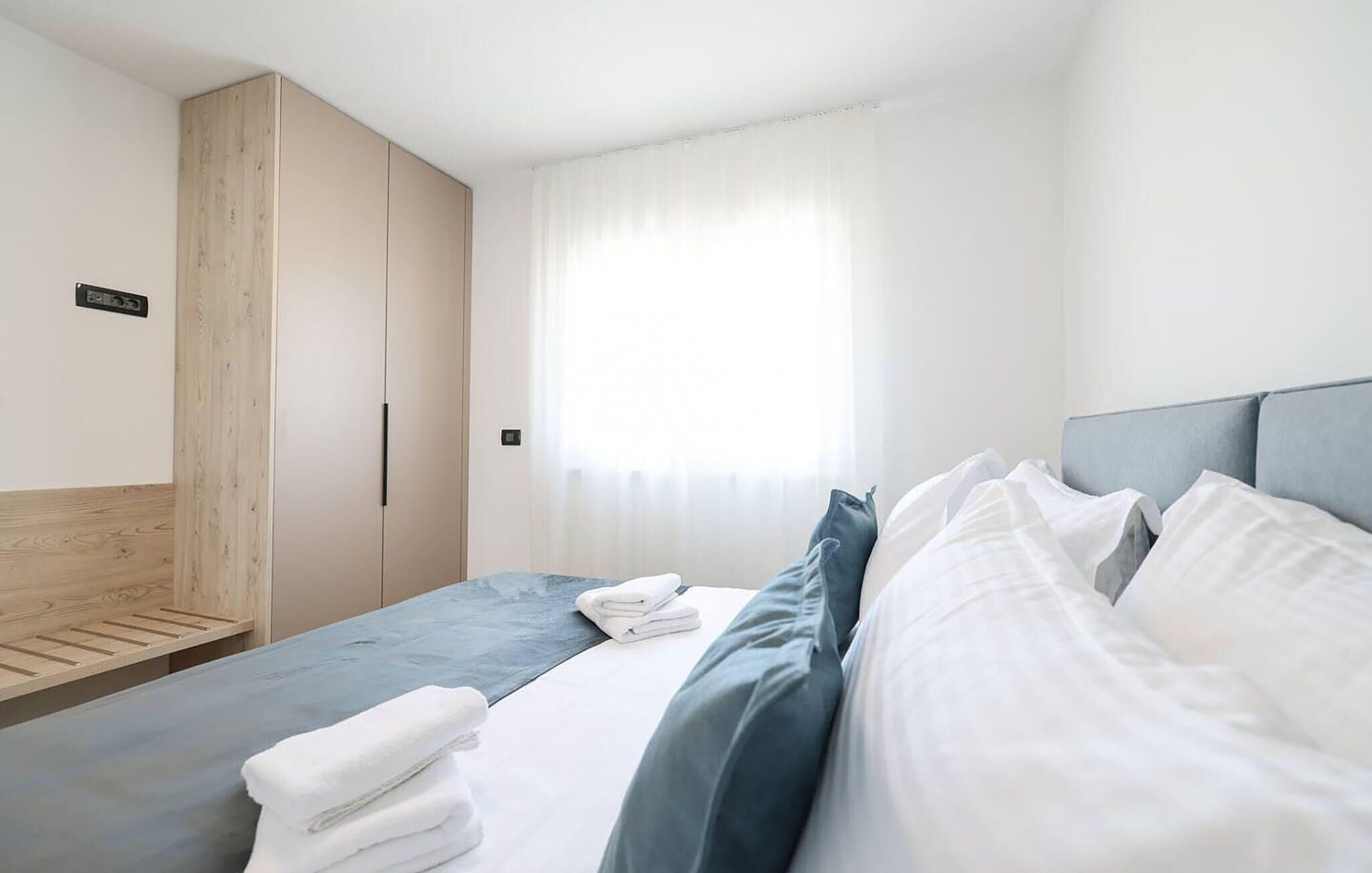 Una camera d'albergo con un letto, un armadio, una finestra con tende e un comodino con asciugamani.