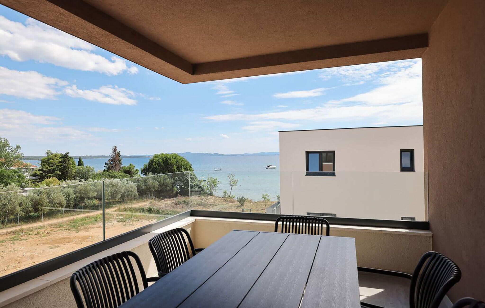 Un balcón con mesa y sillas, con vista a una masa de agua y tierra distante.