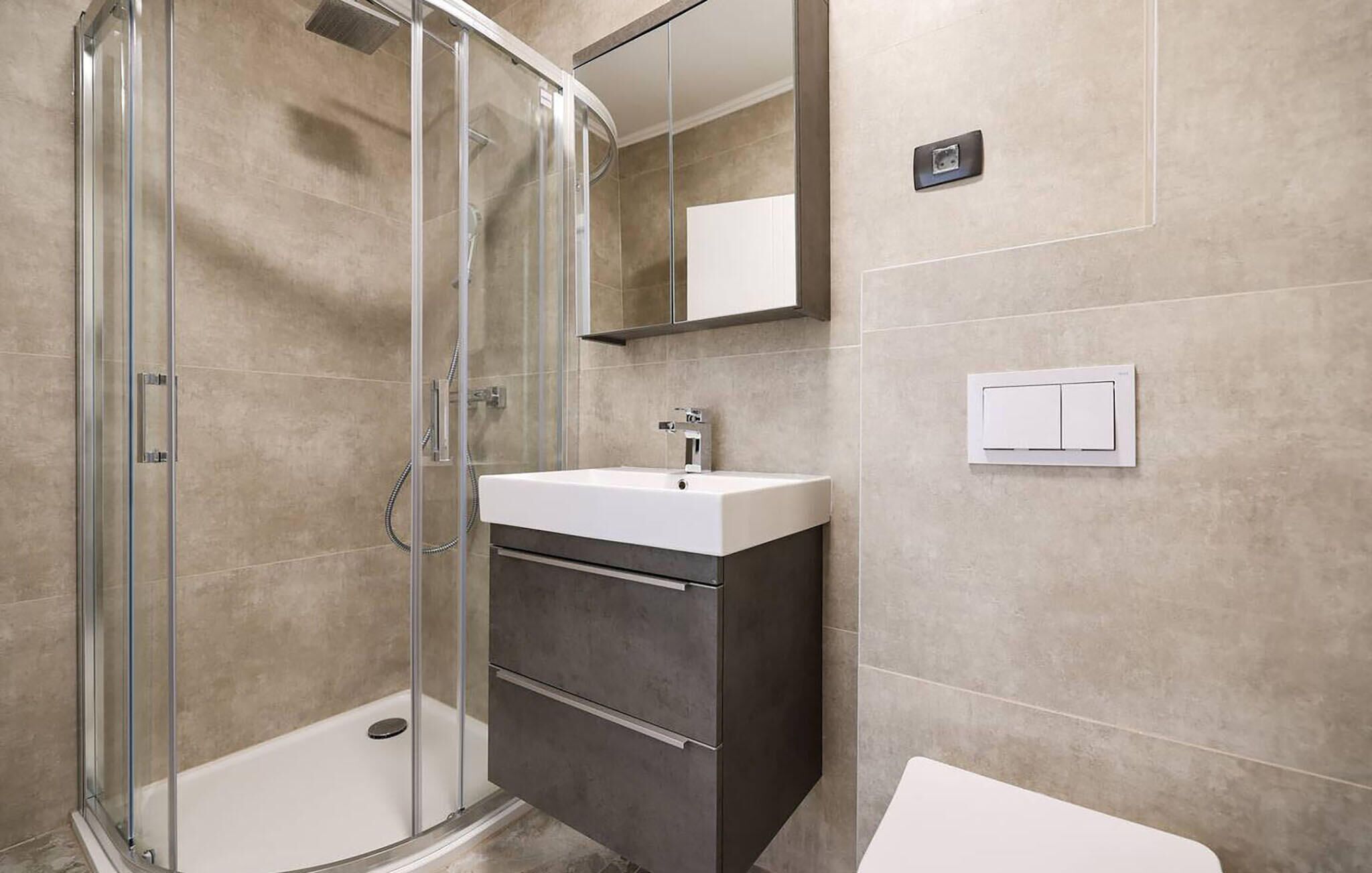 A modern bathroom with a glass-enclosed shower, a white sink, and a dark vanity.