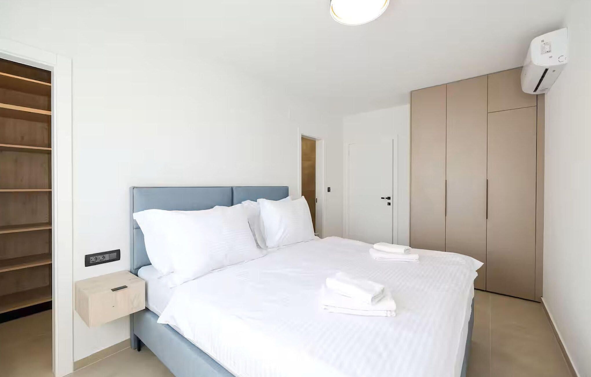 Quarto moderno com cama, mesa de cabeceira, guarda-roupa e estantes embutidas.