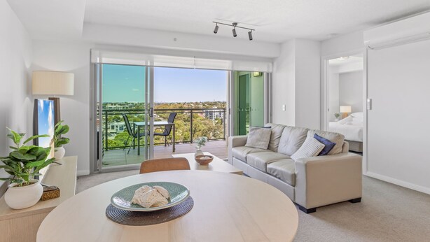 A modern living room with a round table, a sofa, and a balcony with a view. - Seaside Escape With Pool, Balcony and Views (Redcliffe)