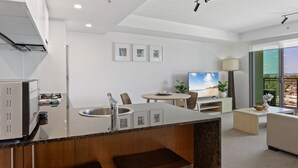A modern kitchen with a built-in island, a dining area with a table and chairs, a sofa, and a TV. - Seaside Escape With Pool, Balcony and Views (Redcliffe)