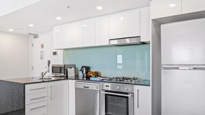 A modern kitchen with white cabinets, stainless steel appliances, and a glass backsplash. - Seaside Escape With Pool, Balcony and Views (Redcliffe)