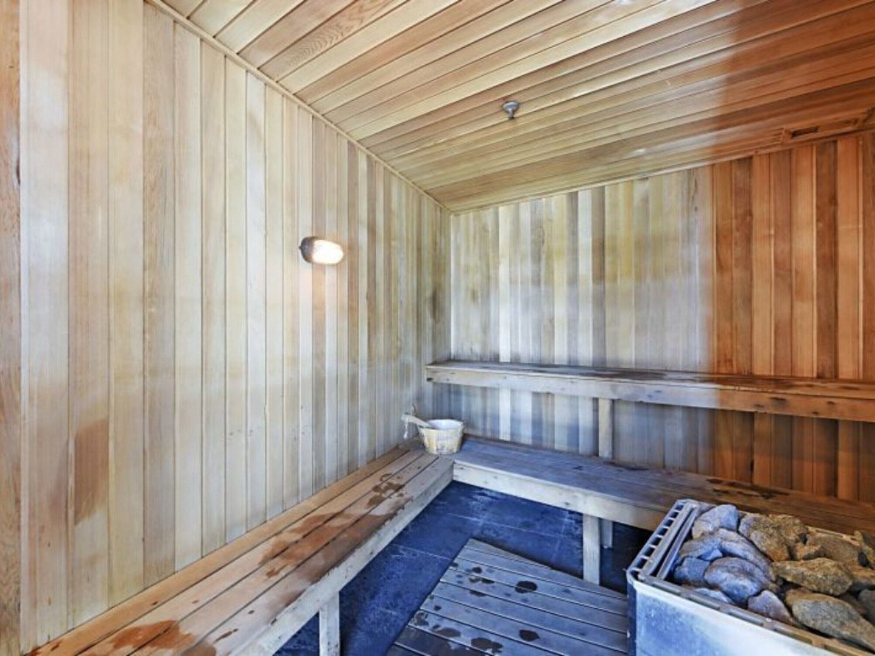 Un sauna avec des bancs en bois et un banc en pierre, un luminaire et un récipient rempli de pierres.