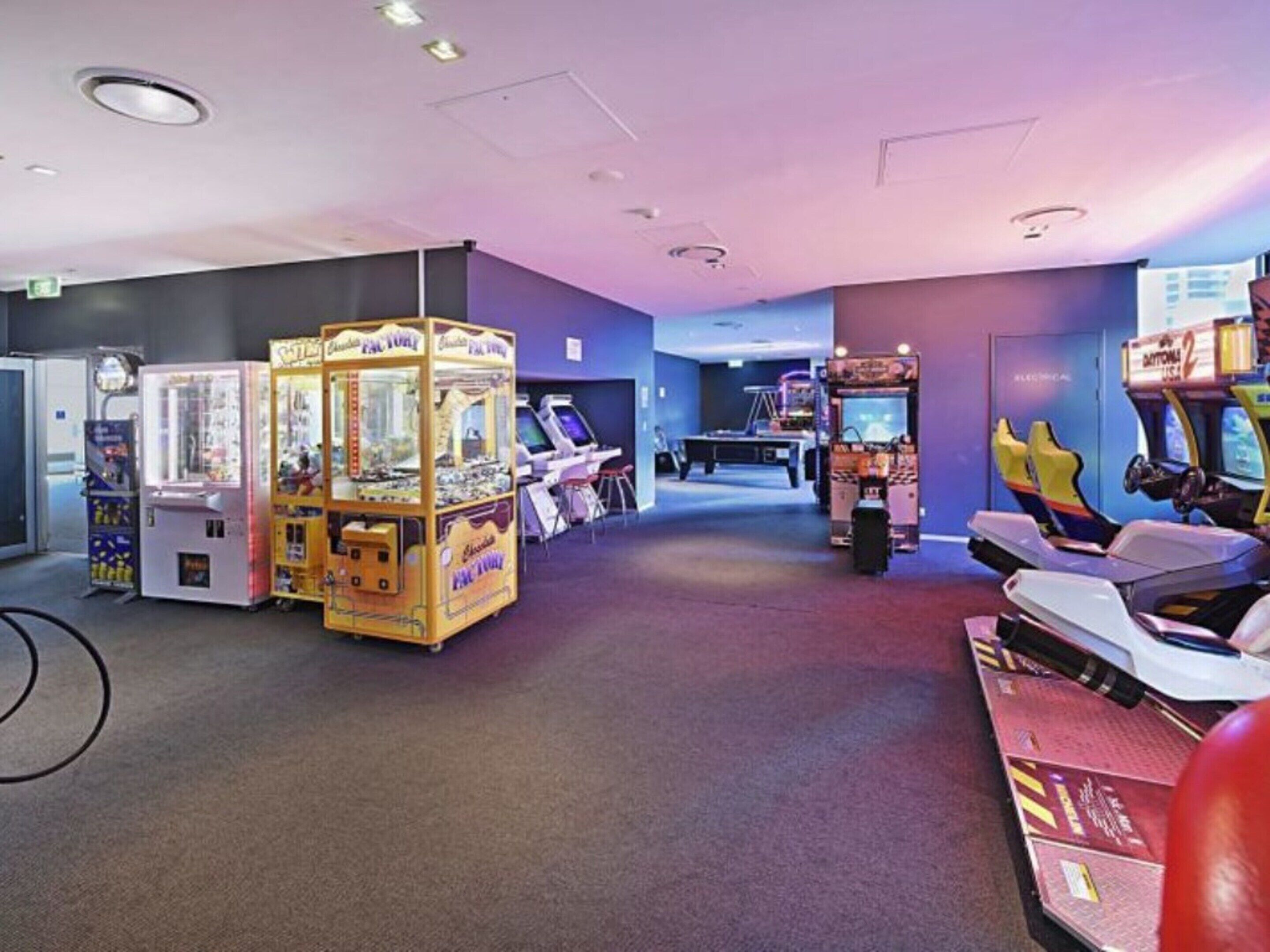 Zona de juegos con máquinas de garra, simuladores de carreras y una mesa de billar.