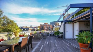 Une terrasse sur le toit, avec une table et des chaises en verre, entourée de plantes en pot et offrant une vue sur le paysage urbain.
