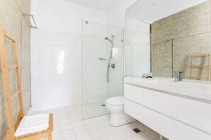 Een moderne badkamer met een glazen douchecabine, een wit toilet en een grote spiegel boven een witte wastafel.
