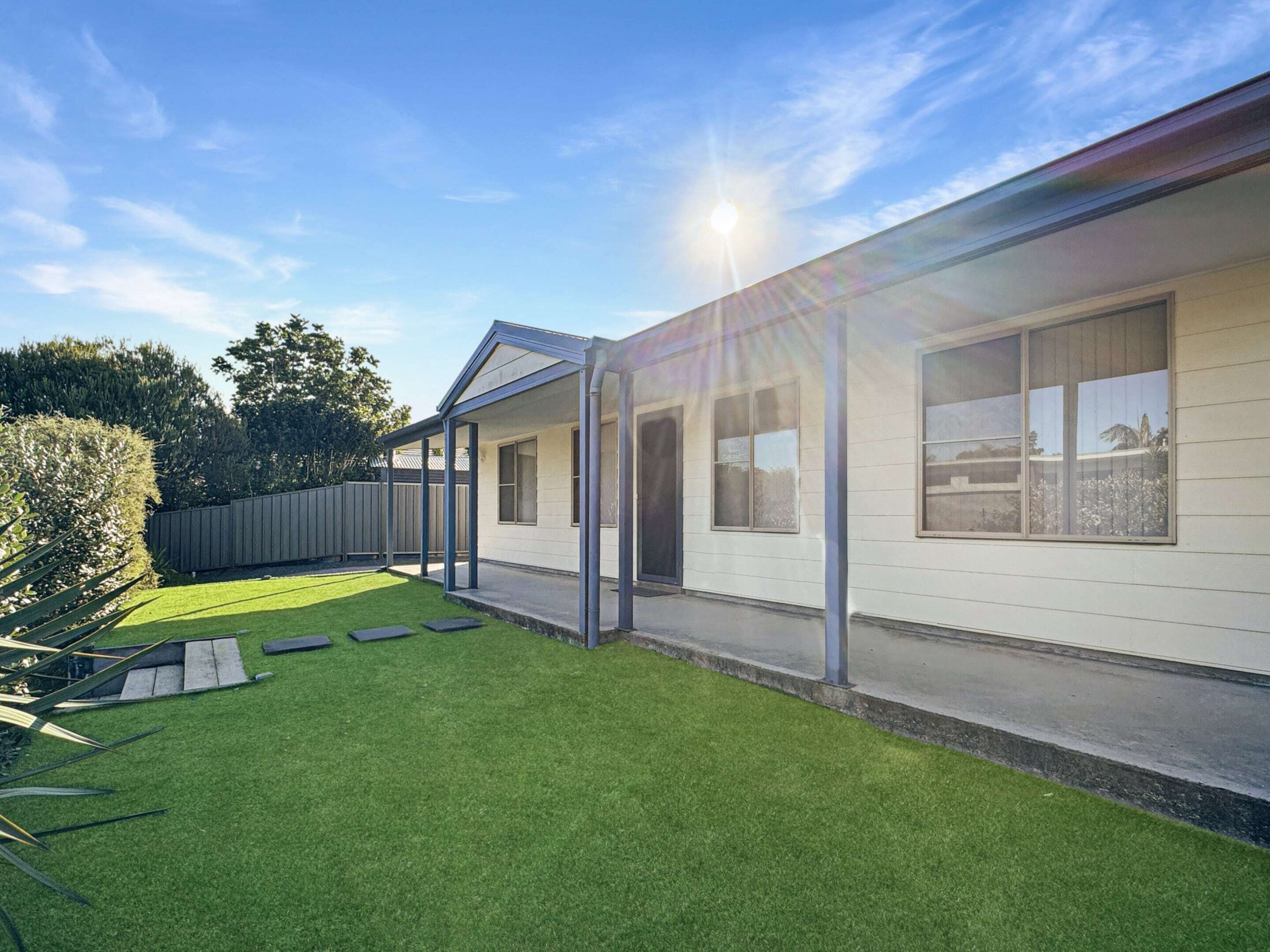 A modern house with a covered patio, a well-maintained lawn, and a wooden fence.