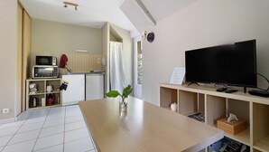 A modern kitchen with a microwave, toaster, and a wooden dining table with a vase. - Studio – Le Clos des Pommiers (Pleudihen-sur-Rance)