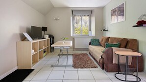 A living room with a sofa, a small table, a TV, and a radiator. - Studio – Le Clos des Pommiers (Pleudihen-sur-Rance)