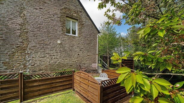 A stone building with a wooden fence, a grassy yard, and a tree with green leaves. - Studio – Le Clos des Pommiers (Pleudihen-sur-Rance)