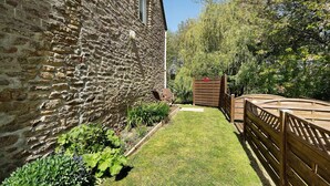 A stone building with a brick wall, a wooden fence, and a grassy area with plants. - Studio – Le Clos des Pommiers (Pleudihen-sur-Rance)