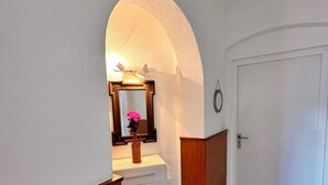 Un corridoio con una parete bianca, una porta in legno e un comò bianco con cassetti.
