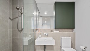 Een moderne badkamer met een douchecabine van glas, een witte wastafel en een toilet.