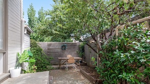 A backyard with a concrete patio, a wooden table, and chairs. There is a wooden fence and a tree with green leaves. - Contemporary 1-bed Unit Near Chapel St (Melbourne)
