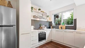 A modern kitchen with white cabinetry, a stainless steel refrigerator, an oven, and a window with plants outside. - Contemporary 1-bed Unit Near Chapel St (Melbourne)