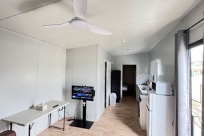 Une chambre d’hôtel compacte dotée d’une kitchenette, d’un téléviseur à écran plat, d’un ventilateur de plafond et d’une fenêtre.