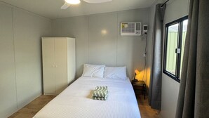 Et soveværelse med seng, garderobeskab, ventilator, klimaanlæg, sengetæppe og et vindue med gardiner.