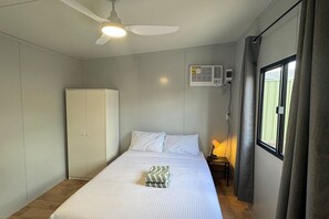 Et soveværelse med seng, garderobeskab, ventilator, klimaanlæg, sengetæppe og et vindue med gardiner.