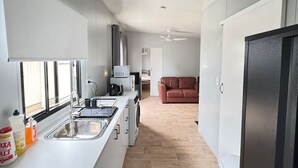 Et moderne køkken med indbygget ovn, mikroovn og vask. Der er et vindue der giver naturligt lys, og en loftventilator er synlig.