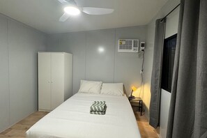 Un dormitorio con cama, armario, aire acondicionado, ventilador de techo y mesita de noche con lámpara.