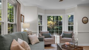 A living room with a green sofa, two armchairs, a coffee table, and a view of greenery through large windows. - Spacious|Close to DT|5 BDRM|4BA|PetsOK (Greenville)