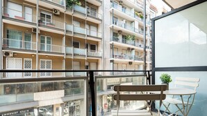 A balcony with a bench and a table, overlooking a multi-story building with balconies and air conditioning units. - Barirooms - District 198 (Bari)