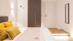 A bedroom with a bed, two pillows, a wardrobe, a door, and a mirror. - Barirooms - District 198 (Bari)