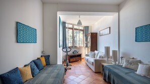 Un salon avec un canapé, une table basse et un téléviseur. Il y a une fenêtre avec des rideaux, une lampe et un cadre photo accroché au mur.
