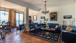 Un salon spacieux avec un grand canapé, un coin repas comprenant une table et des chaises, et une vue sur la mer grâce à de grandes fenêtres.