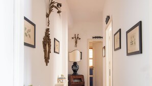 Un couloir avec une table en bois, un vase rempli de fleurs, des tableaux encadrés accrochés aux murs et une lampe.
