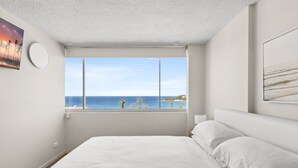 Een slaapkamer met een groot bed, een raam met uitzicht op de zee en een schilderij aan de muur.