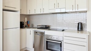 Een moderne keuken met witte kastjes, een vaatwasser, een oven en een koffiezetapparaat.