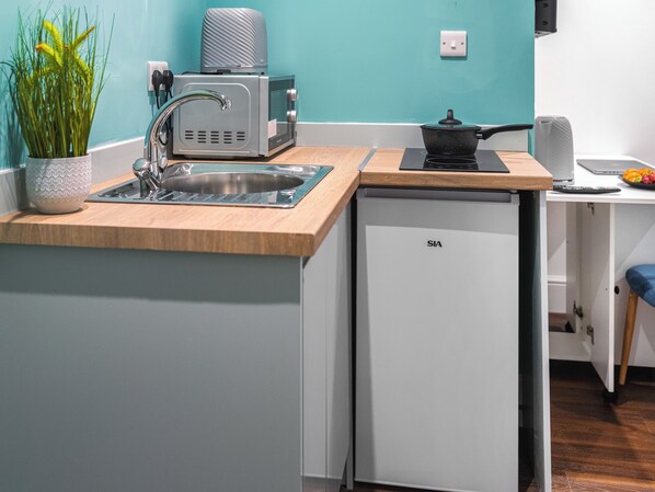 Una cocina compacta con un lavamanos, un microondas y un refrigerador pequeño.