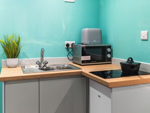 A kitchen with a sink, a microwave, a pot on an induction cooktop, and a potted plant.