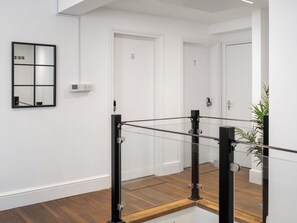 Un interior moderno con barandilla de vidrio, paredes blancas y suelo de madera.