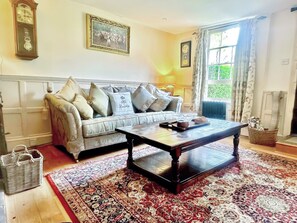 A living room with a sofa, a coffee table, a clock, and a window with curtains.