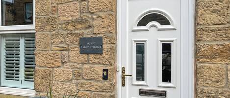 Fachada de piedra con una puerta blanca, una placa con la inscripción "ARDBEG 7 ARGYLE TERRACE" y una ventana con contraventanas.
