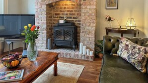 A cozy living room with a brick fireplace, a television, a sofa, and a coffee table with a vase of flowers. - 2 bedroom accommodation in Hexham (Hexham)