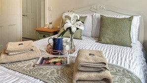 A neatly made bed with a floral-patterned bedspread, two towels, a vase with white flowers, and a magazine on the bed. - 2 bedroom accommodation in Hexham (Hexham)