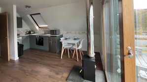Une cuisine moderne dotée d’une cuisinière intégrée, d’un coin repas avec une table et des chaises, et d’une grande fenêtre offrant une vue sur l’extérieur.