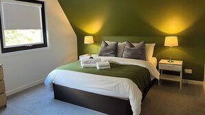 Une chambre à coucher avec un lit, deux tables de chevet, une fenêtre et un luminaire au plafond.