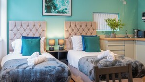 A hotel room with two beds, a small kitchen area, and a dining table.