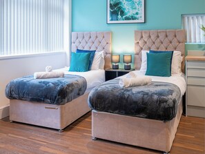 Habitación de hotel con dos camas, cada una con cabecero tapizado, y una mesita de noche con lámparas entre ellas.