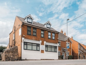 A two-story brick building with a white facade, a ground-floor shop, and a sign for Hilltop Serviced Apartments.