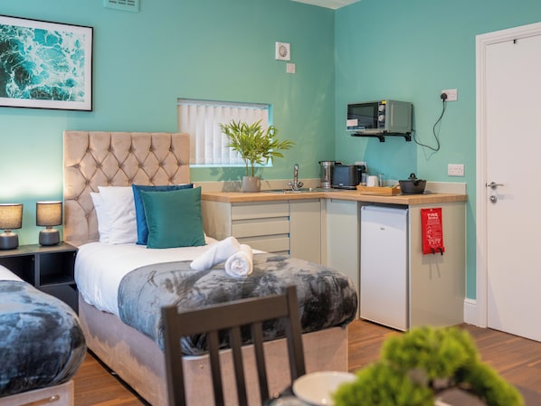 A compact hotel room with a bed, a small kitchenette, a dining area, and a bathroom.