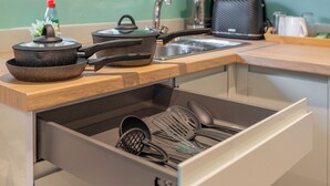 A kitchen with a wooden countertop, a stove, a sink, and a drawer with kitchen utensils.
